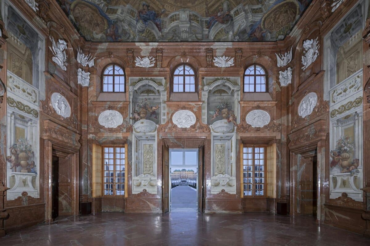 Ornate hall with frescoes and tall windows.